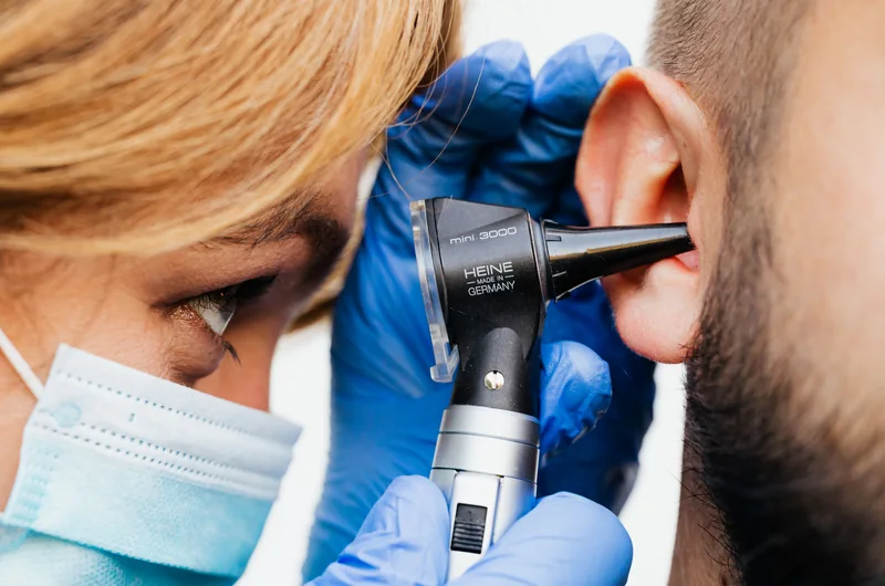 Audiologist examining a patient's ear with an otoscope, financed by Alphaeon Credit